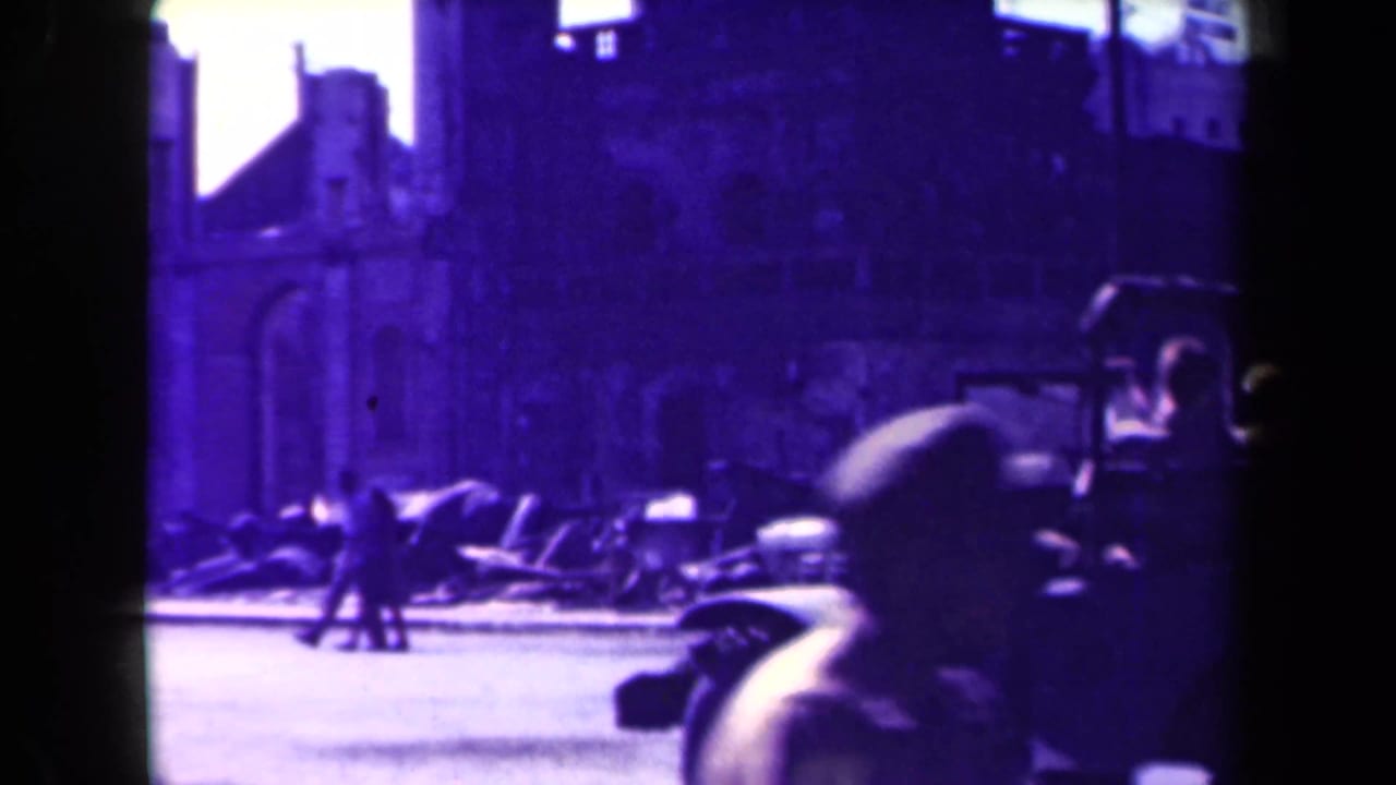 Jeep at the right edge of a street scene with pedestrians and damaged buildings behind it.