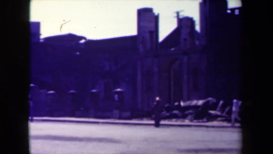 1944 Manila wide street frame with damaged buildings, debris near the curb, pedestrians, and a strong purple 8mm color cast.