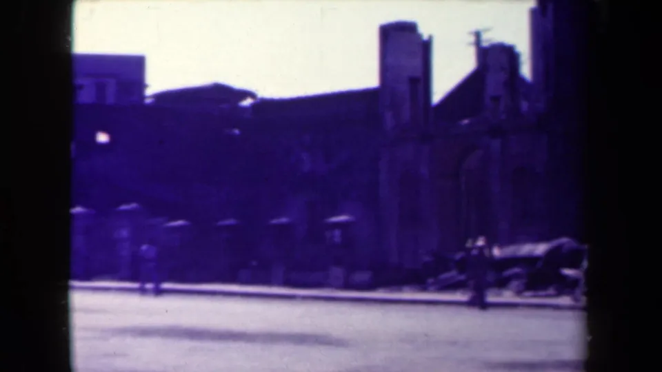 1944 Manila home-movie frame showing a street beside weathered masonry, dark arch framing, and a small pedestrian for scale.