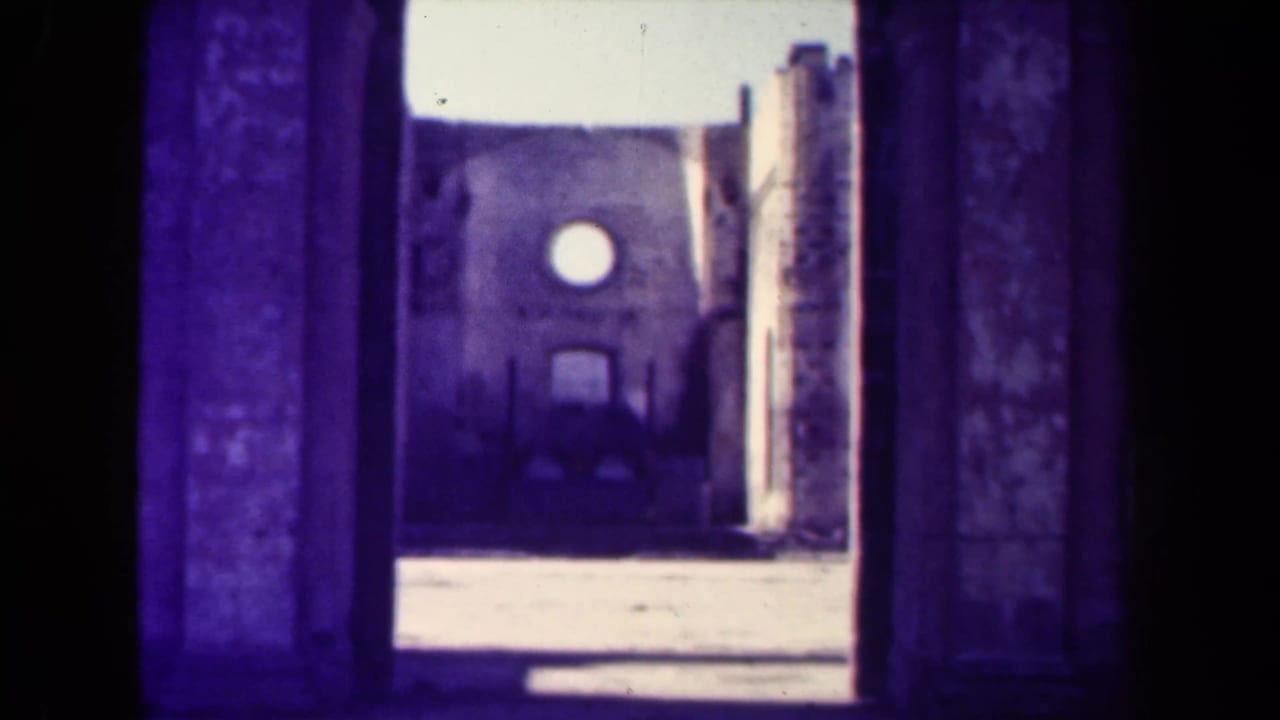 Large shadowed archway frames a weathered facade with a circular window and rough stone walls.
