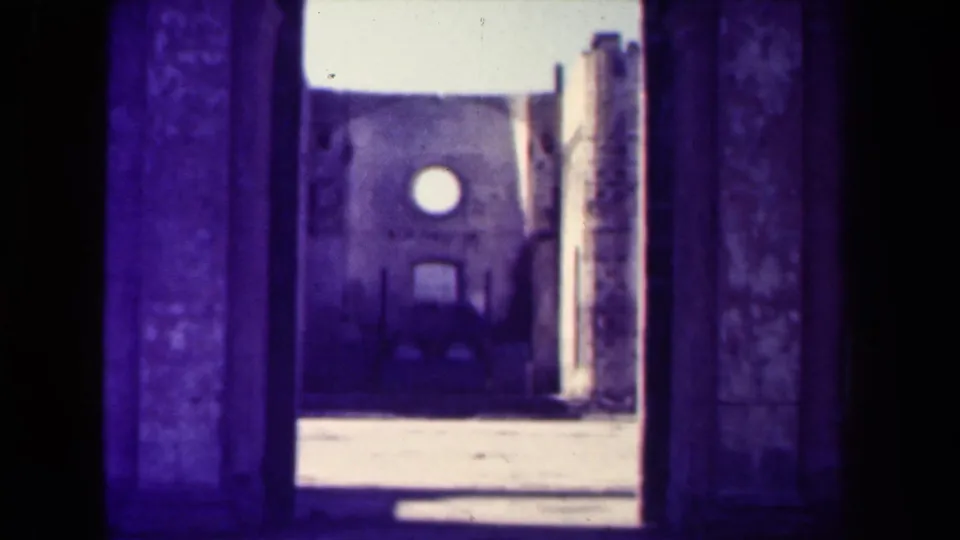 1944 Manila frame looking through a dark stone arch toward a church-like facade with a round window and damaged masonry.