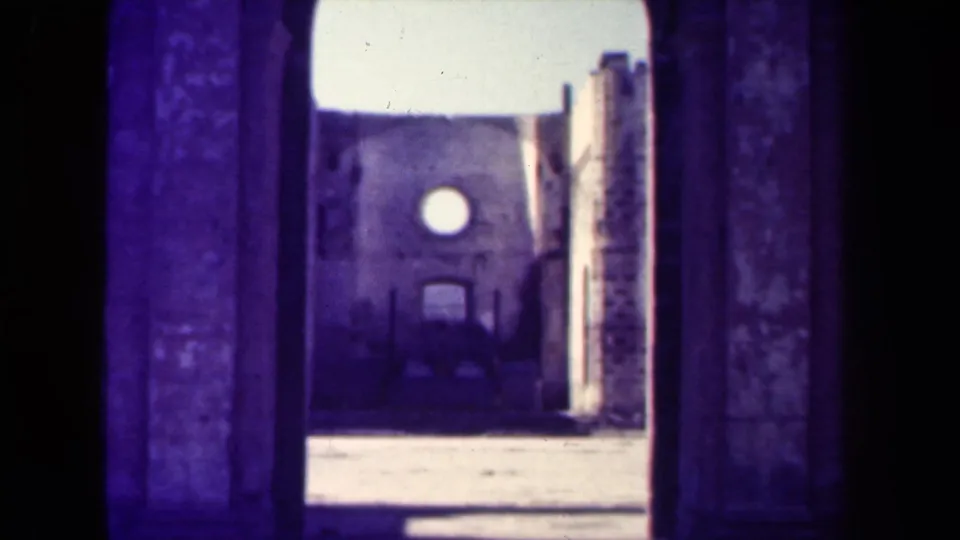 1944 Manila home-movie view through a stone entrance toward a weathered church-like facade with a circular window.