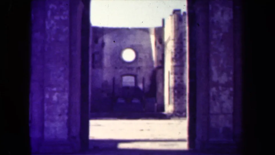 Final 1944 Manila frame of a purple-tinted 8mm view through an arch toward a weathered facade with a round window.