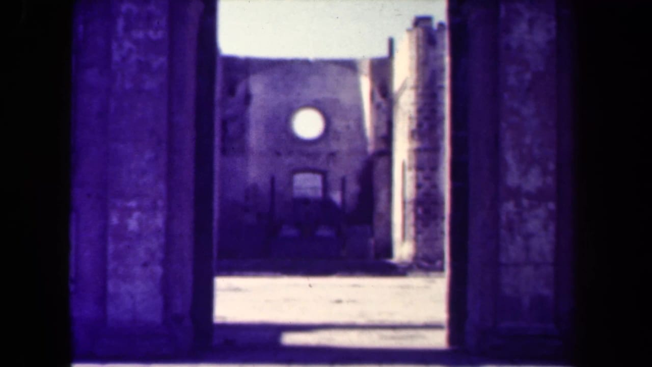 1944 Manila 8mm frame looking from a dark doorway toward a damaged masonry structure with a round opening.