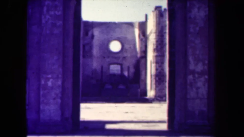 1944 Manila 8mm frame looking from a dark doorway toward a damaged masonry structure with a round opening.