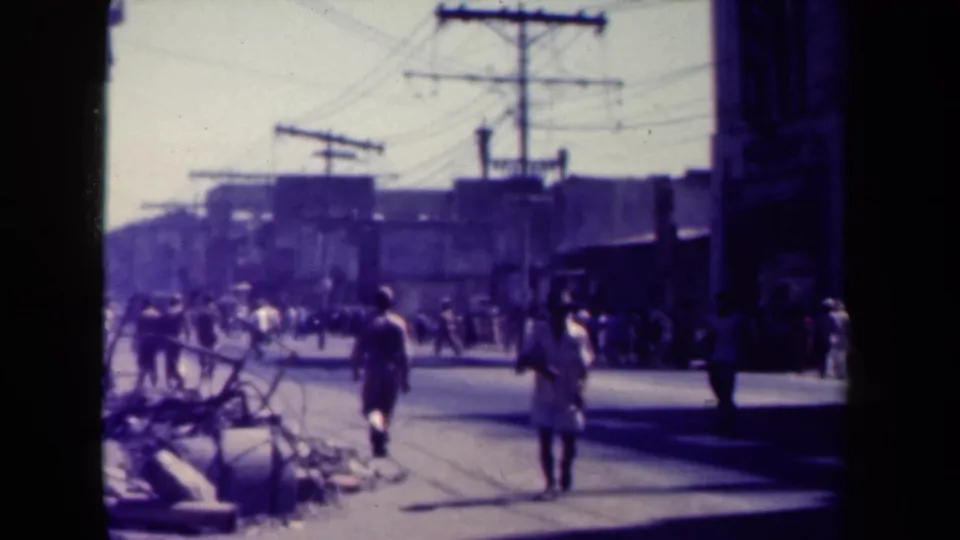 1944 Manila street view with pedestrians moving past roadside debris, utility poles, and distant buildings.