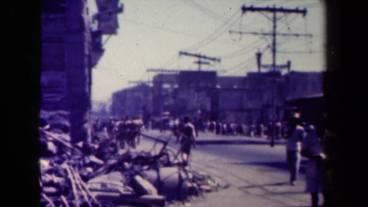 War-damaged street with rubble, utility poles, and pedestrians in the distance.
