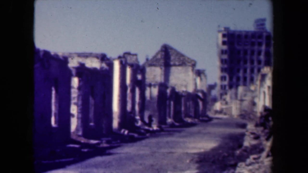 Manila ruins in 1944, with a road curving past roofless masonry walls and a taller damaged structure beyond.