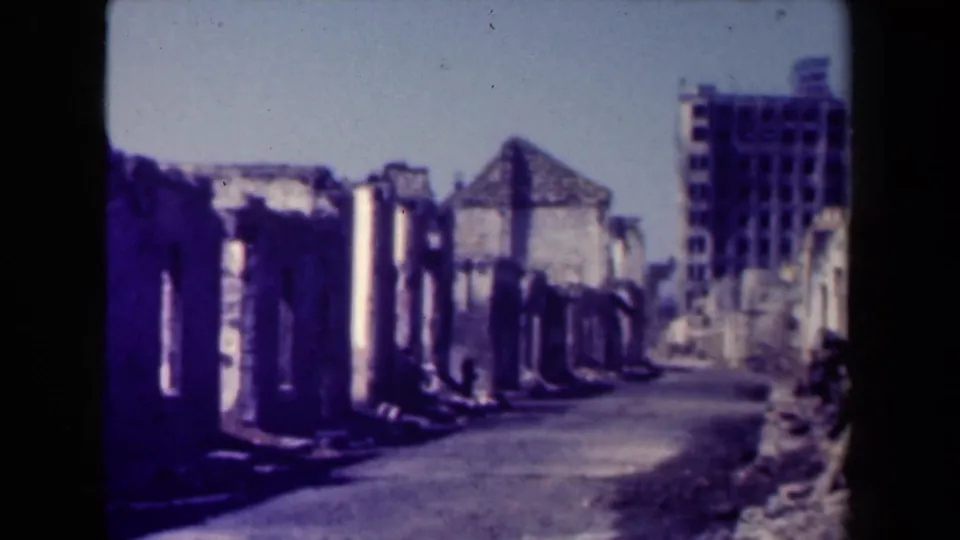 Manila ruins in 1944, with a road curving past roofless masonry walls and a taller damaged structure beyond.