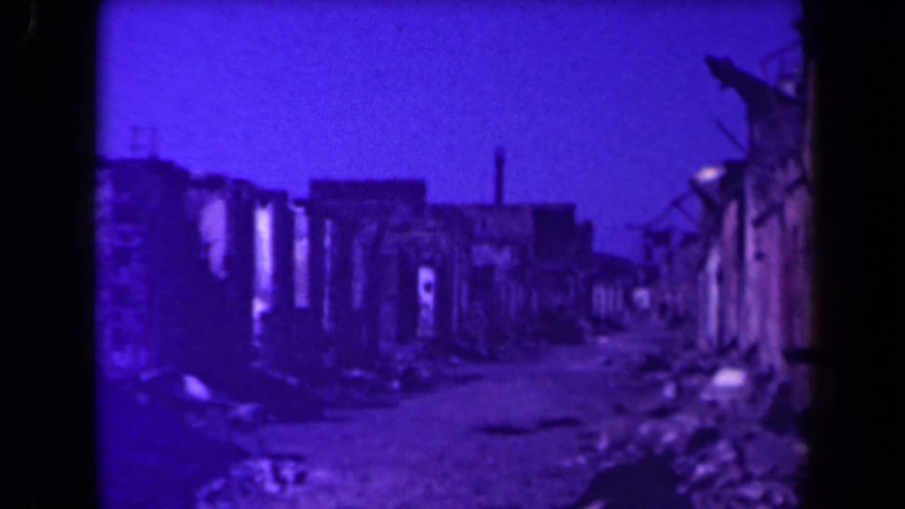 Rubble-strewn lane between damaged buildings with a dark purple cast.
