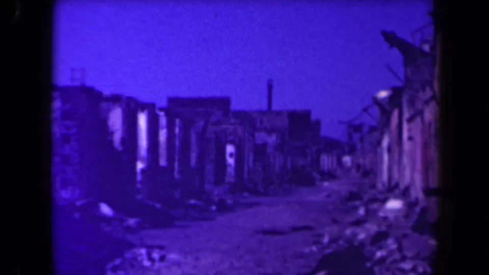 1940s Manila footage showing a debris-filled lane bordered by heavily damaged buildings under a purple film tint.