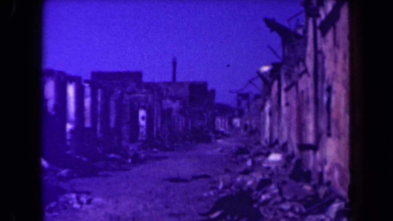 Damaged urban lane with collapsed walls and debris along both sides.