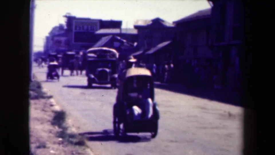 1940s Manila street life with pedestrians, a small car in the foreground, and larger vintage vehicles moving along the road.