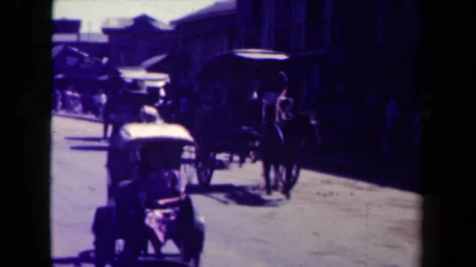 1944 Manila street view with a horse-drawn carriage, an early automobile, pedestrians, and shaded building fronts.