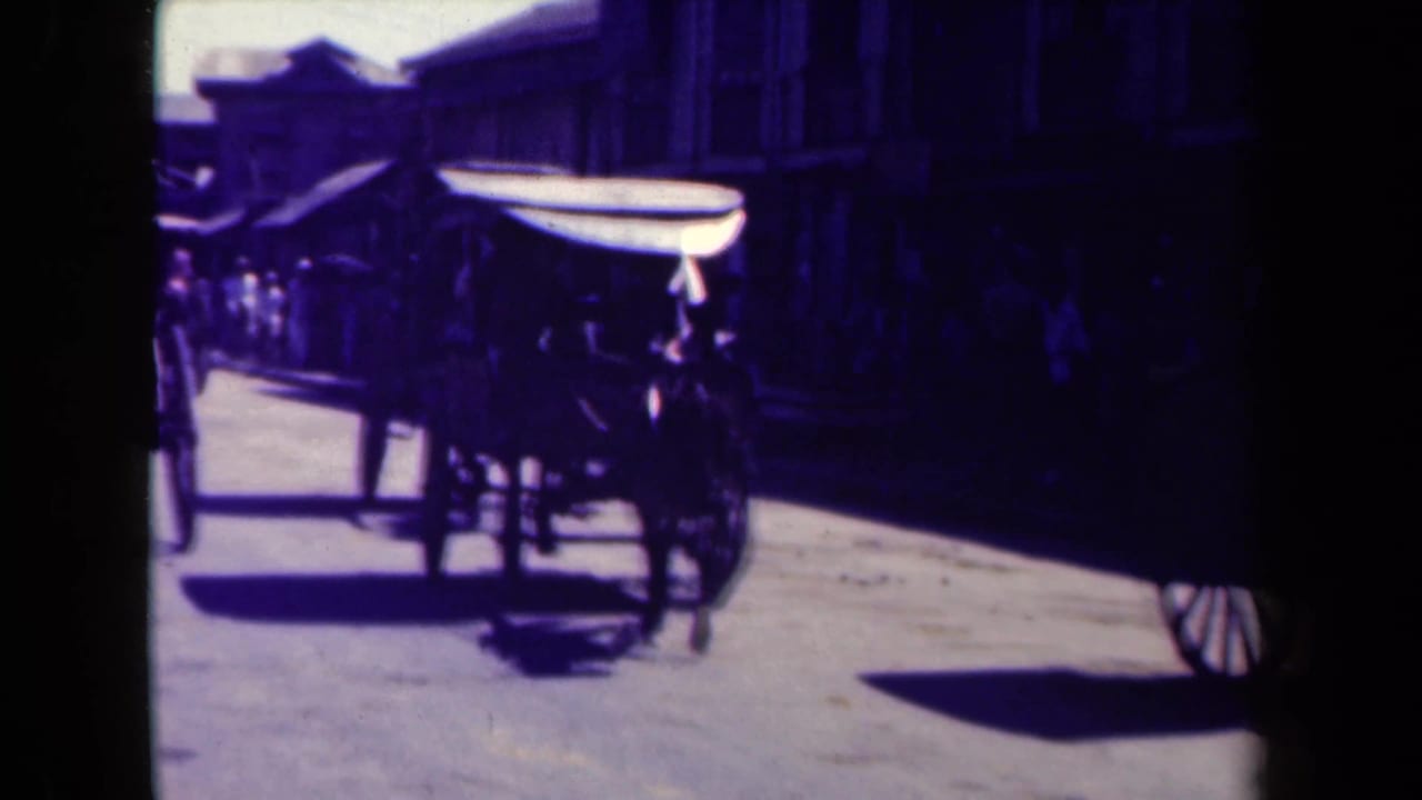 1944 Manila street view with a dark truck passing near a cart-like vehicle and shadowed buildings.