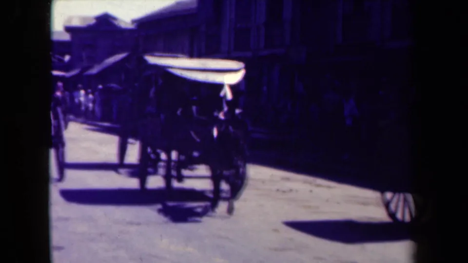 1944 Manila street view with a dark truck passing near a cart-like vehicle and shadowed buildings.