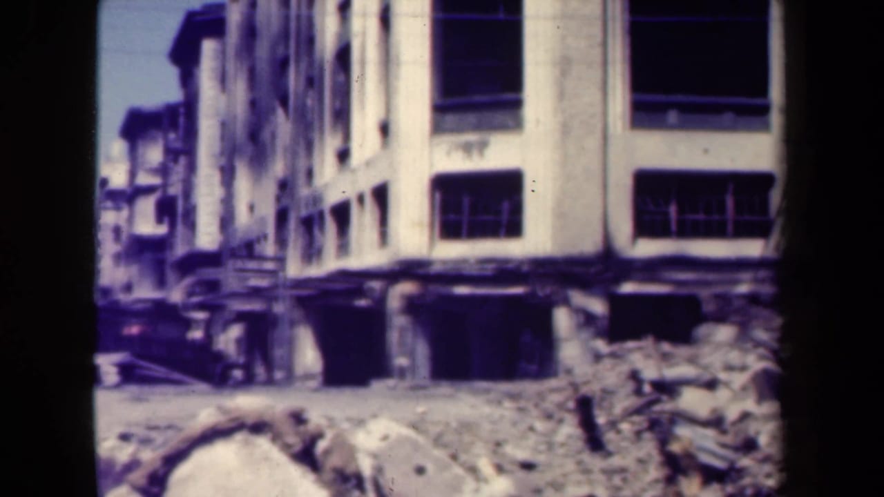 Dark truck beside a damaged white building with rubble in front.