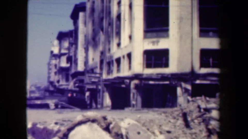 1944 Manila view of a damaged white building, a dark truck, and foreground rubble under bright daylight.