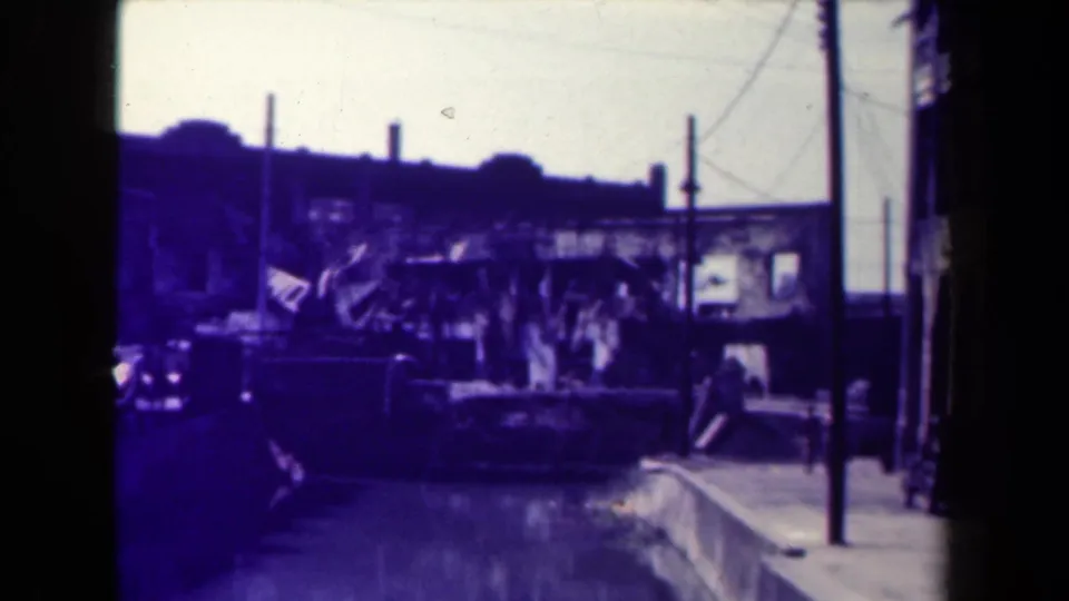 Wider 1944 Manila street view with pedestrians and vehicles near a curb or bridge-like edge, seen through faded 8mm color.
