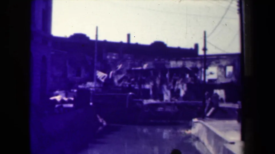 1940s Manila street view with older vehicles, pedestrians, utility poles, bright sky, and darkened edges from the 8mm scan.