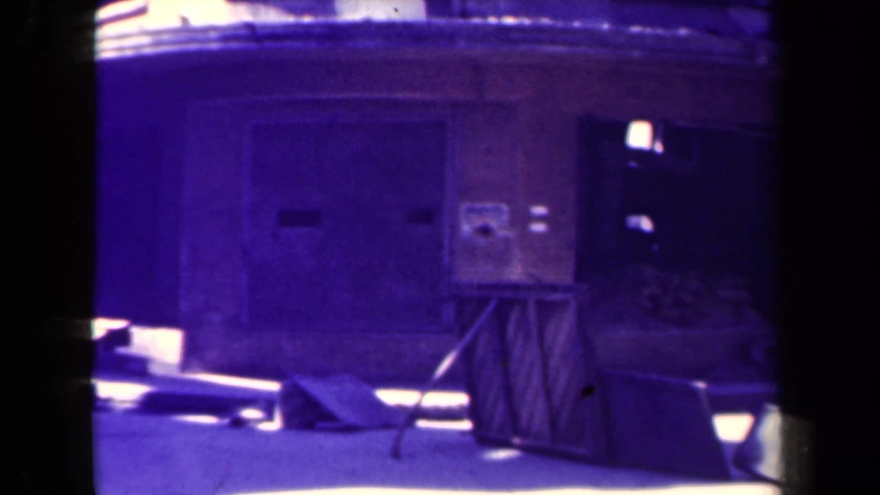 Closed wooden stall beside a dark doorway, with bright sun patches and debris on the ground.