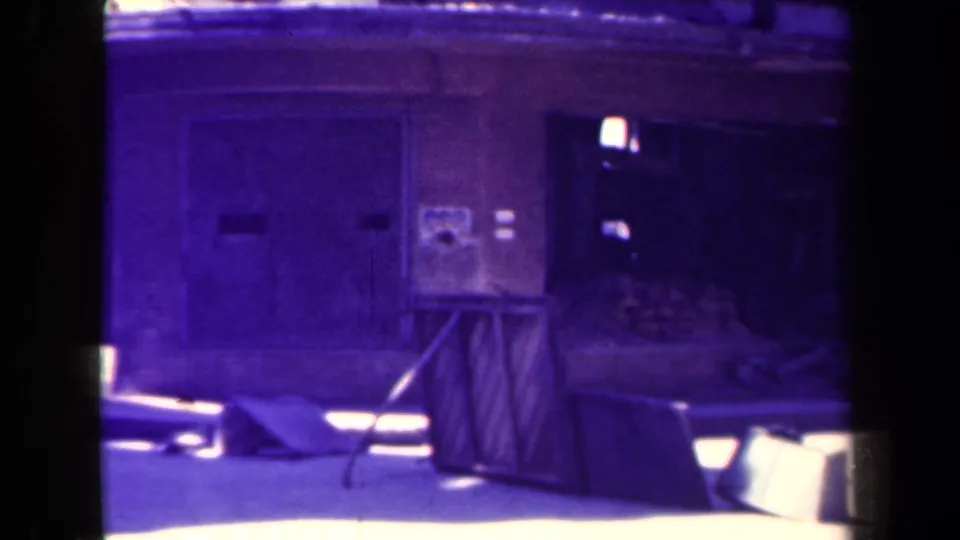1944 Manila storefront detail with a closed wooden stall, arched wall, dark entrance, posted paper, loose boards, and bright pavement glare.