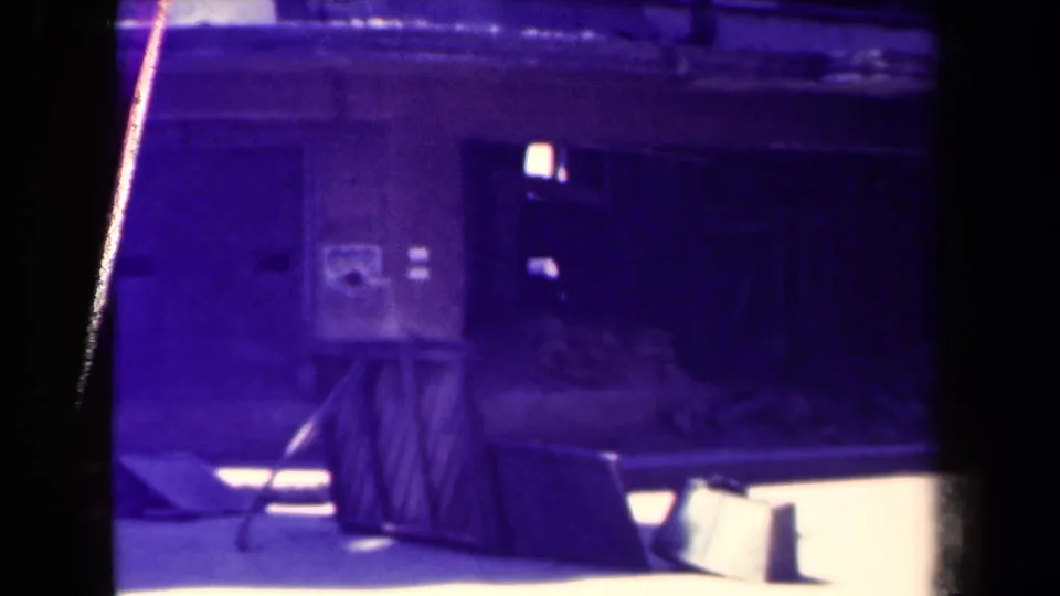 Final 1944 Manila frame showing the closed wooden stall, shadowed doorway, wall poster, debris, and aged purple-blue 8mm color shift.