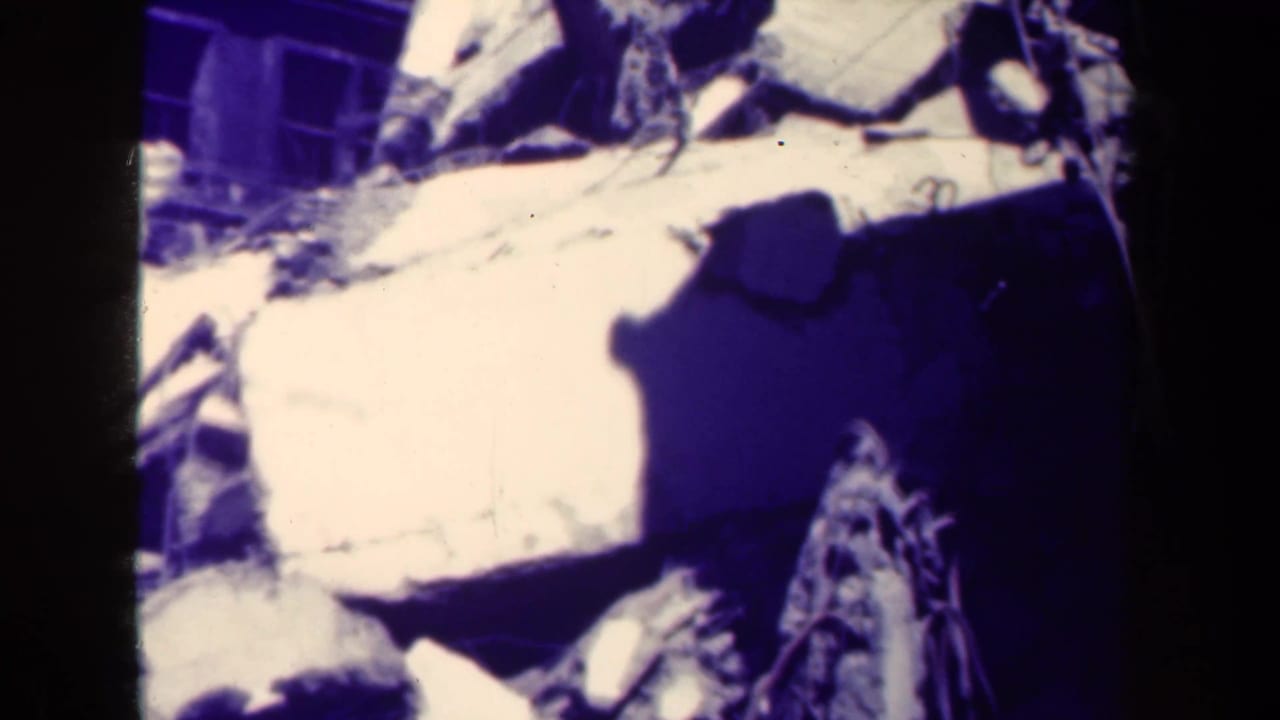 Close view of pale rubble, broken slabs, and dark shadow beside a damaged wall or window area.
