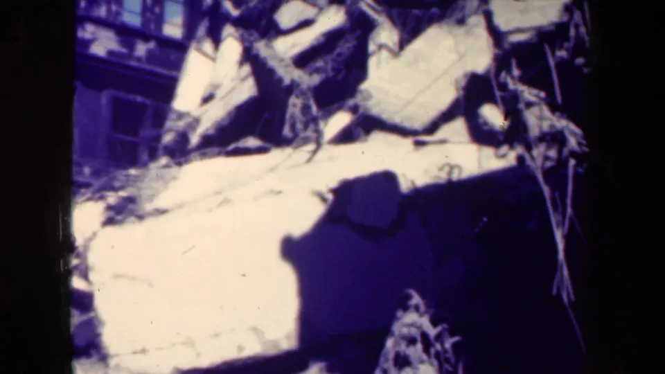 1944 Manila 8mm frame showing collapsed masonry and tangled debris near a damaged building exterior.
