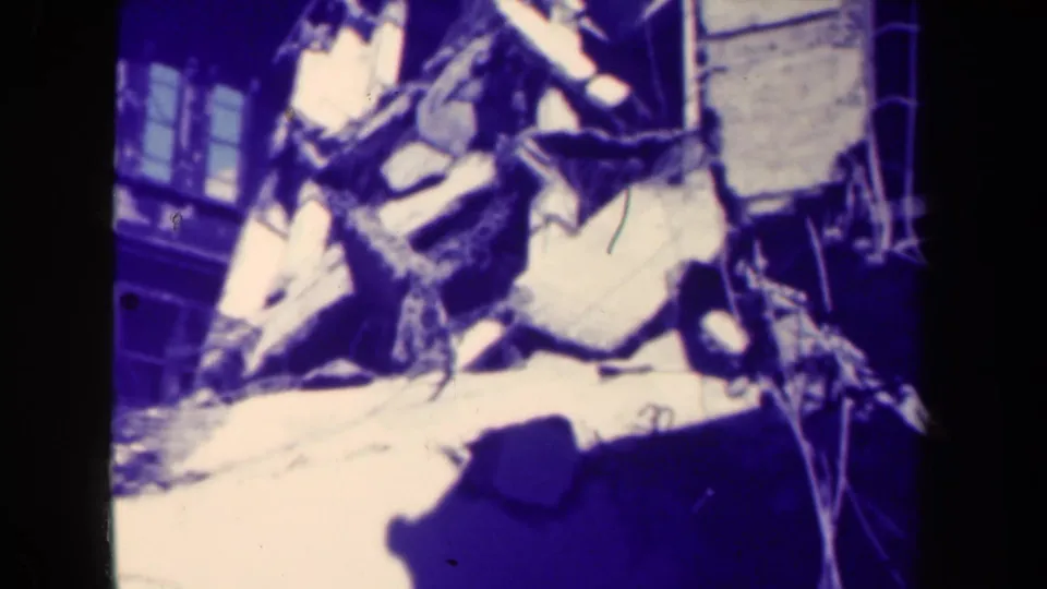 1944 Manila 8mm frame showing a pile of concrete rubble and bent debris near a damaged building facade.