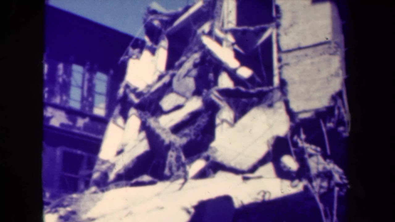 Pile of broken concrete and twisted debris against a damaged wall and building windows.