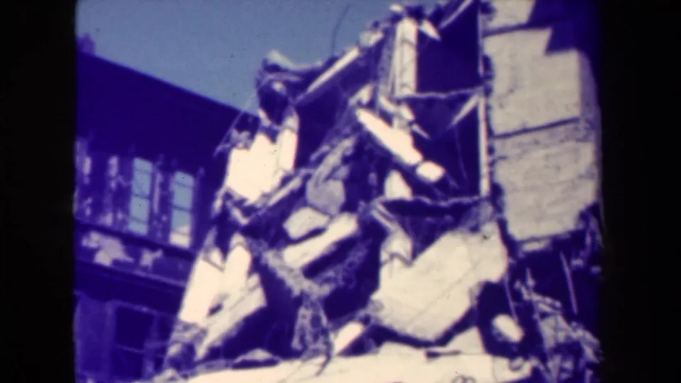 1944 Manila 8mm frame showing the camera moving upward across rubble toward a damaged building edge.