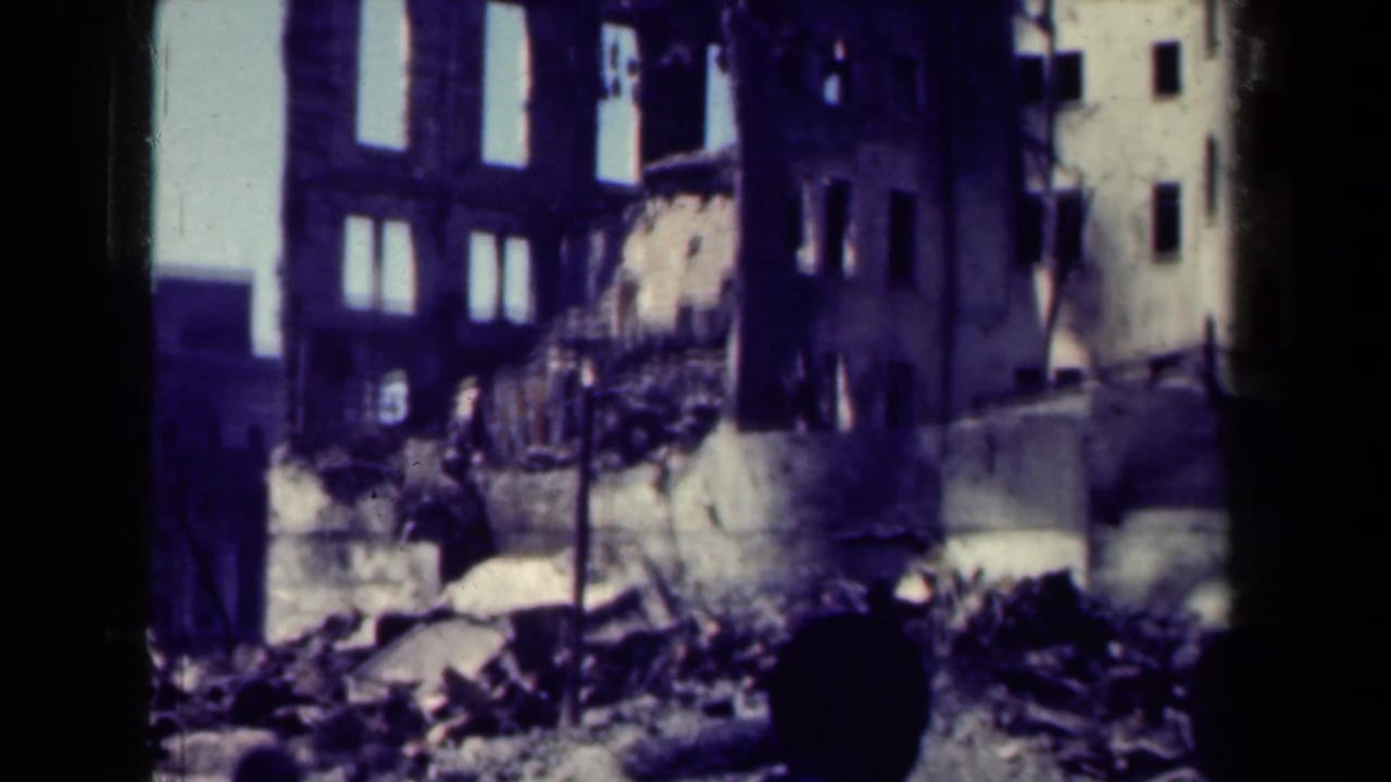 Ruined multi-story building with rubble below and a dark human silhouette in the foreground.