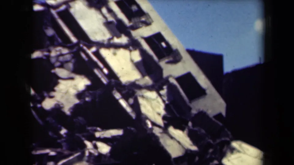 1944 Manila frame showing a damaged facade with tilted concrete sections, empty window openings, and rubble in the foreground.