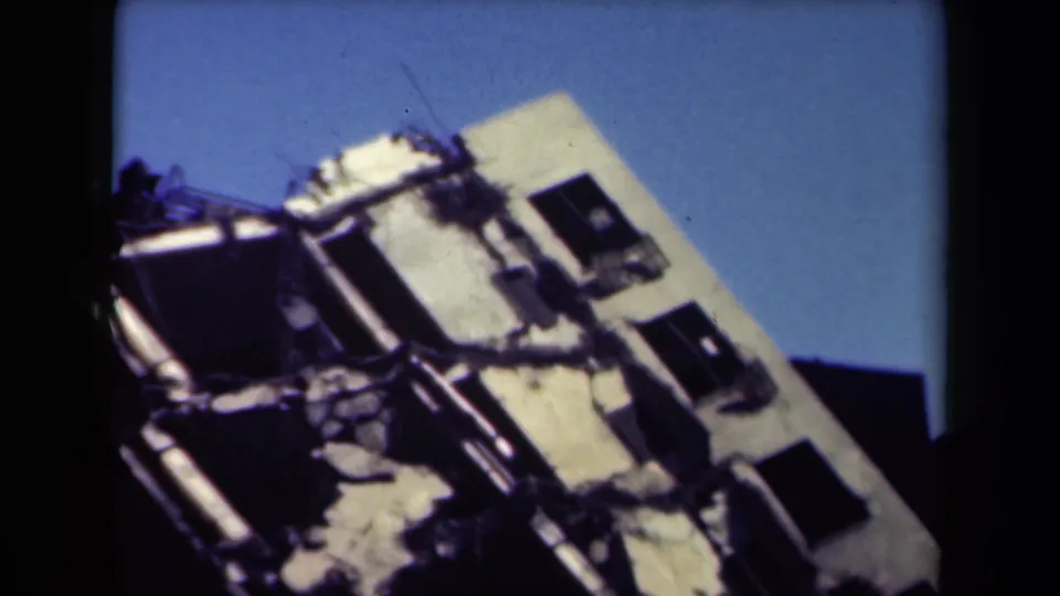 1944 Manila 8mm frame with a tilted handheld view of damaged walls, dark window openings, rubble, and clear blue sky.