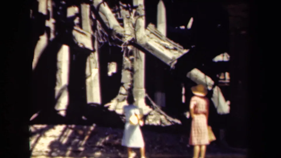 1944 Manila frame showing two women in period dresses near a heavily damaged building with exposed beams, rubble, and deep shadows.