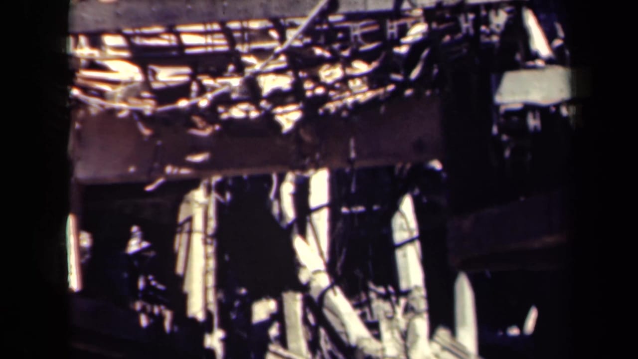 Collapsed building section with twisted beams, broken concrete, and dark structural openings.