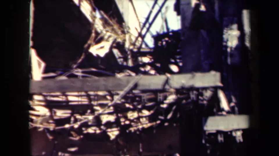 1944 Manila 8mm frame showing burned rubble, collapsed beams, and dark structural remnants under bright light.