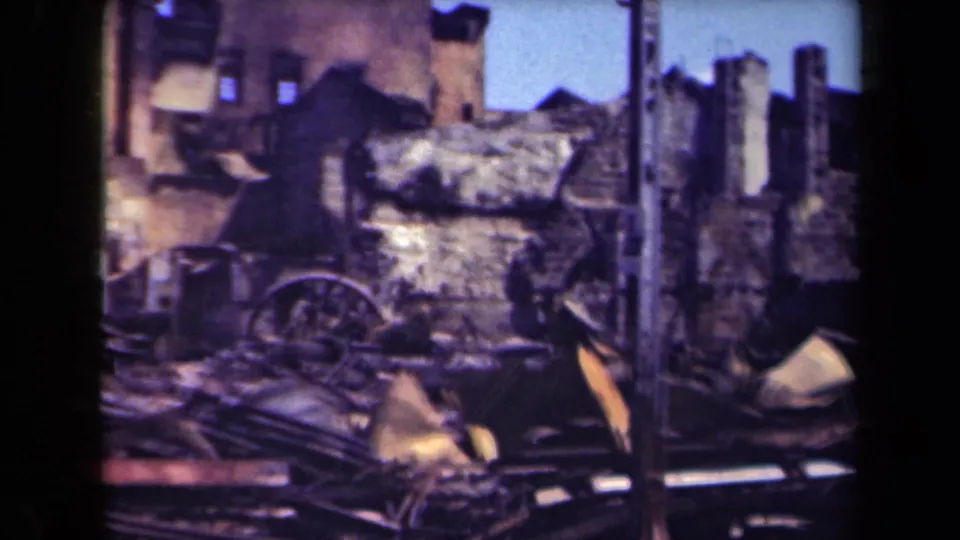 1944 Manila home-movie frame showing burned walls, a wagon wheel, metal scraps, and rubble across the ground.