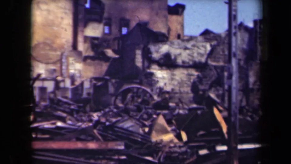 1944 Manila 8mm frame showing a roofless damaged structure, charred debris, and a wagon wheel in the foreground.