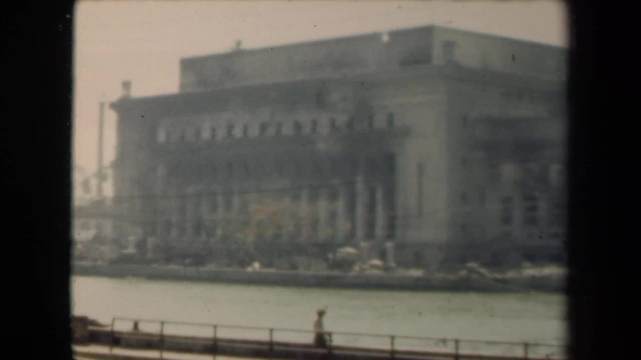 Distant neoclassical building across water with railing and a pedestrian in the foreground.