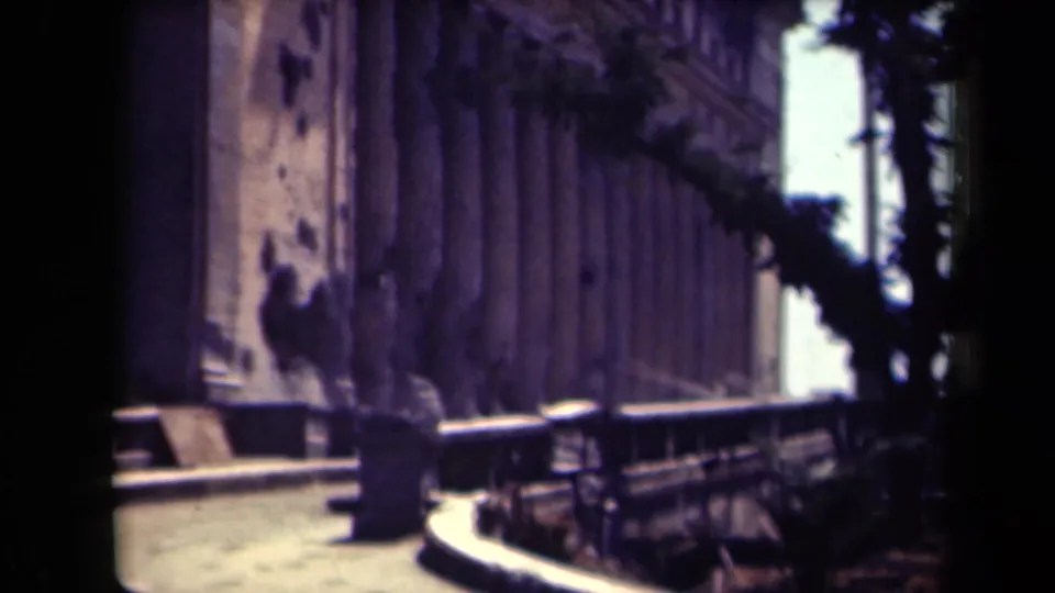 1944 Manila frame showing a shaded building-side walkway with benches, trees, and indistinct people near the facade.