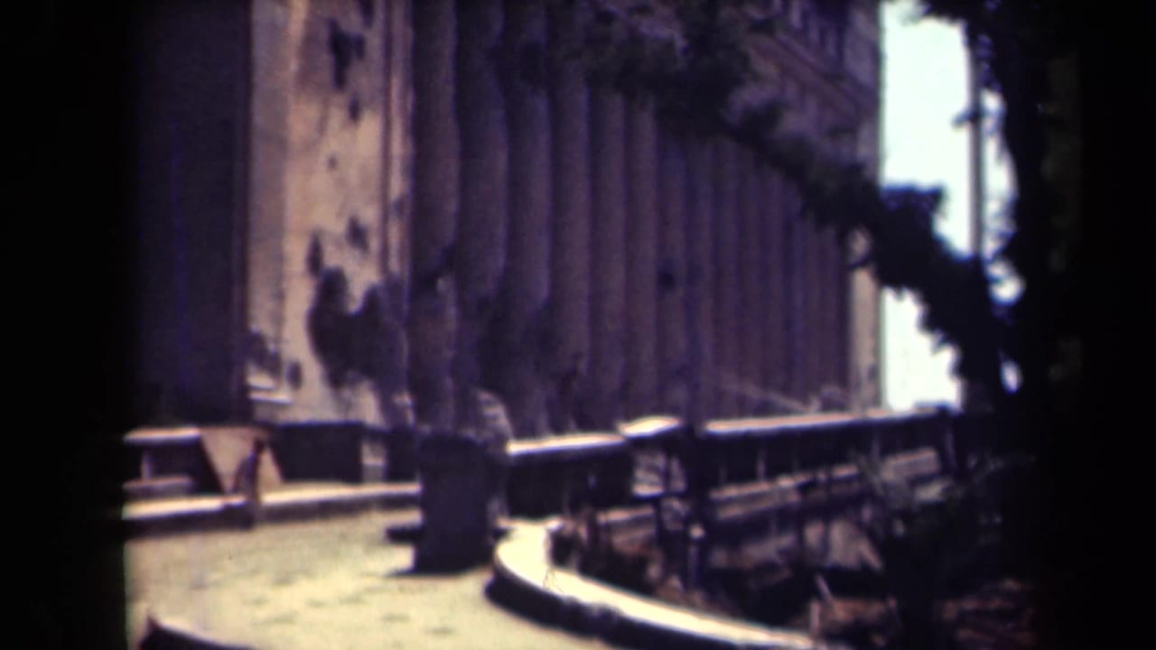 1944 Manila frame of the columned building from the side, showing weathered walls, a curving path, and dark tree shadows.