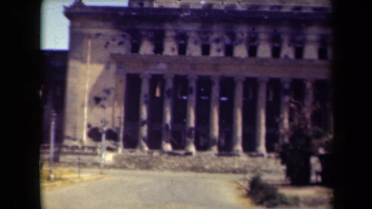 Columned building facade with visible damage and a paved foreground.