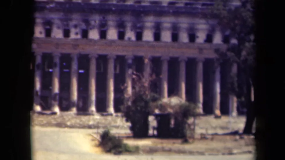 1944 Manila 8mm frame showing the damaged lower and upper portions of a classical columned building behind a paved foreground.