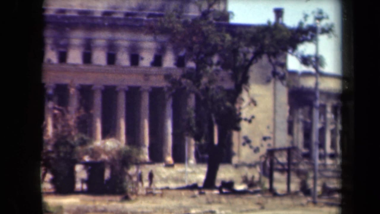 Columned building and adjacent rounded corner seen through trees.