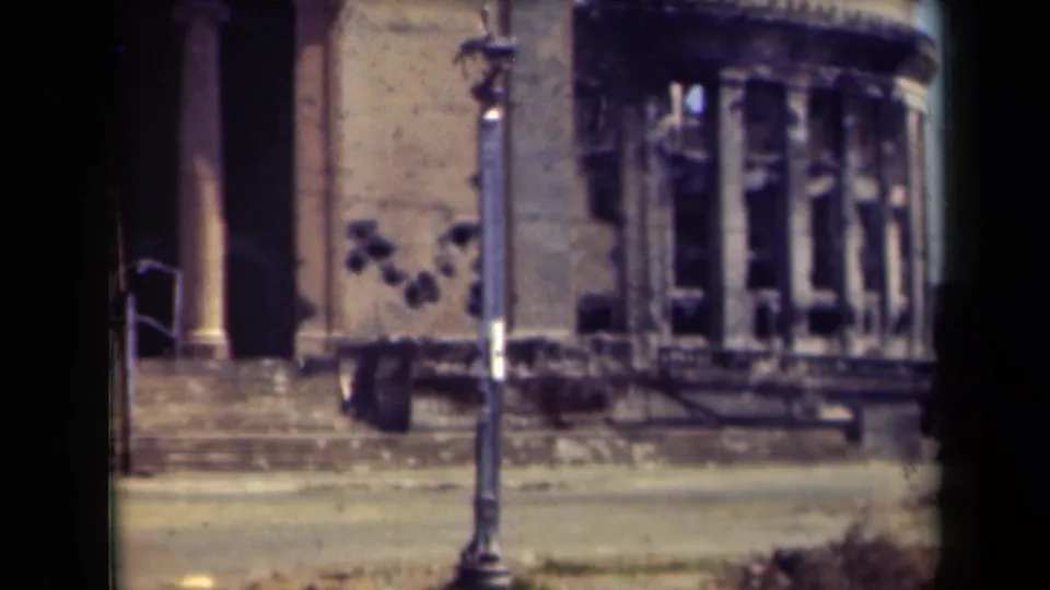 1944 Manila frame showing the building entrance, rounded damaged window bay, lamppost, steps, and quiet street from an 8mm handheld viewpoint.