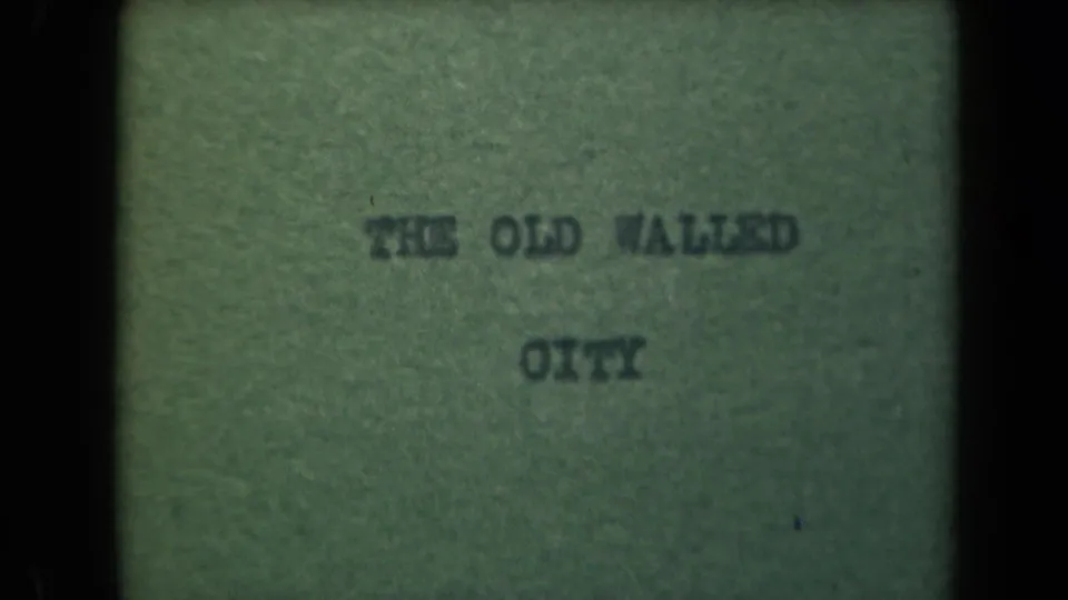 1940s 8mm frame showing a typed THE OLD WALLED CITY title card, softened by faded color and visible film grain.