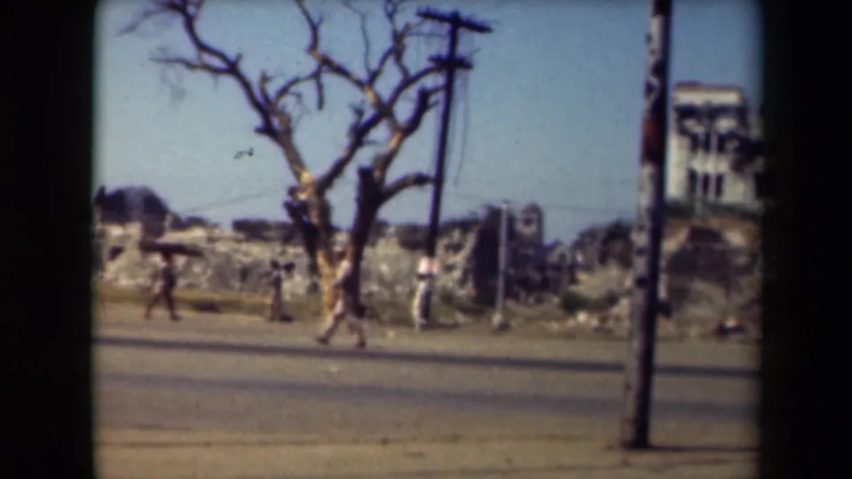 Manila street scene from the 1940s showing pedestrians near a bare tree, utility poles, road surface, and ruined buildings.