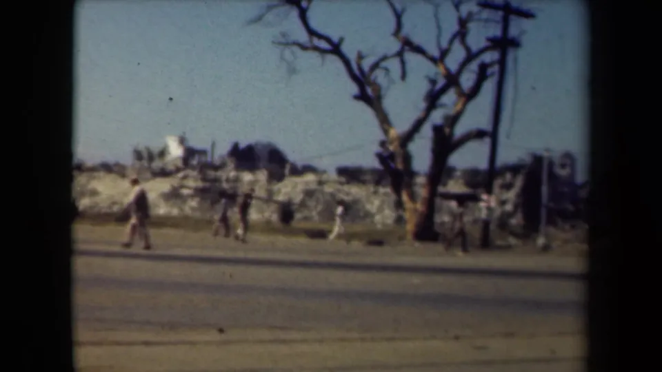 In the 1944 Manila footage, workers and civilians walk along a road in front of rubble, damaged buildings and a bare roadside tree.